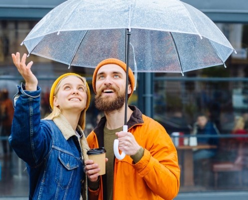 Hipster couple under umbrella in rainy spring cold weather