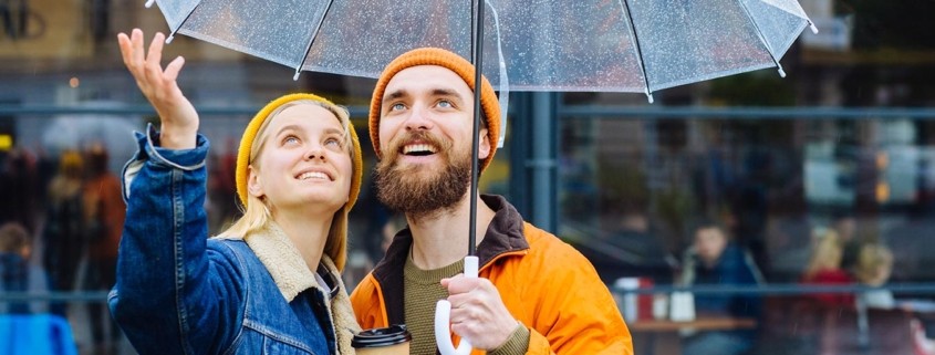 Hipster couple under umbrella in rainy spring cold weather