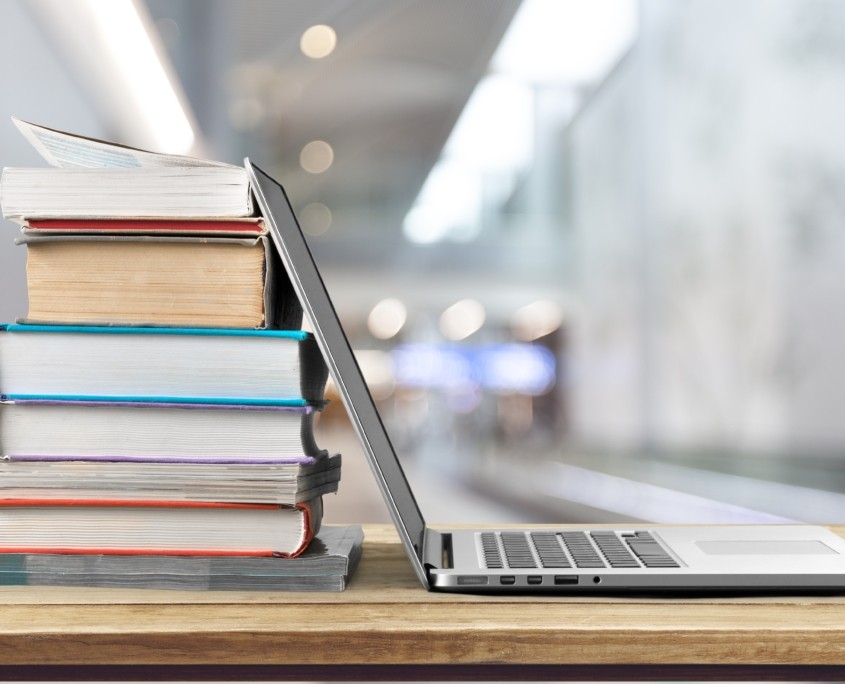 Stack of books with laptop on wooden table