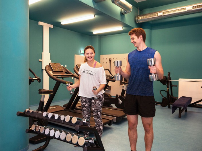 studenten-fitnessraum-training Studenten trainieren gemeinsam mit Hanteln im Fitnessraum.